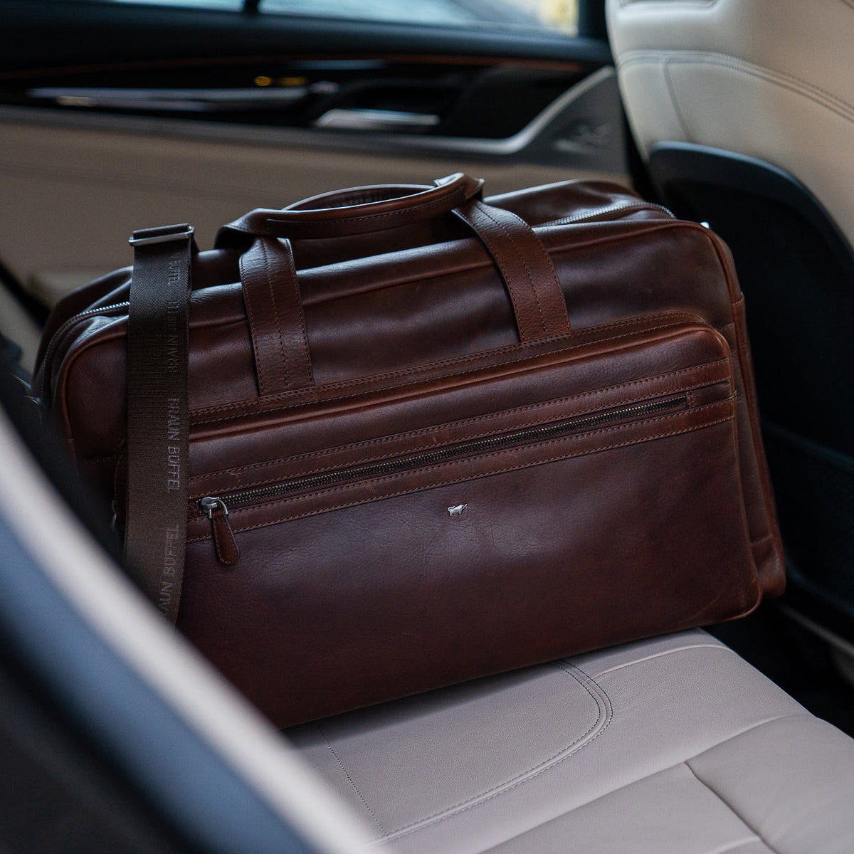 Eine braune Leder-Reisetasche liegt auf der Rückbank eines Autos